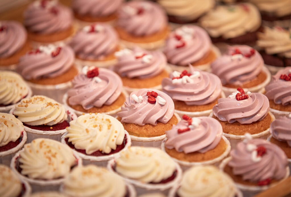 Reihen von Cupcakes mit gewirbeltem lila-weißem Zuckerguss, garniert mit kleinen rot-weißen Verzierungen.