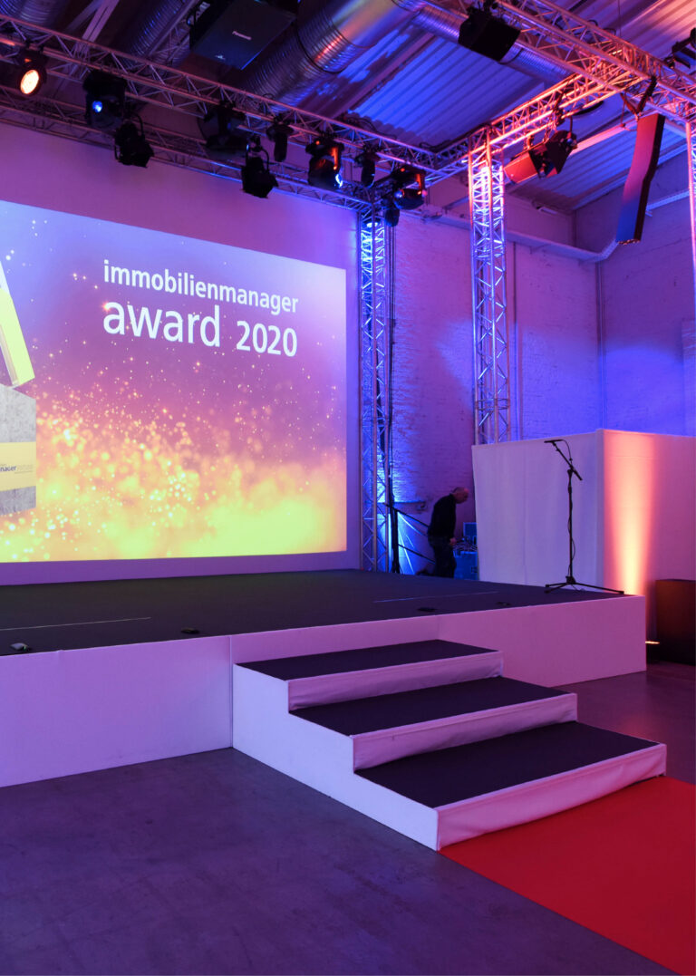Bühnenaufbau mit Leinwand zum immobilienmanager award 2020 und farbenfroher Eventbeleuchtung im Dock 2 in Köln für Events.