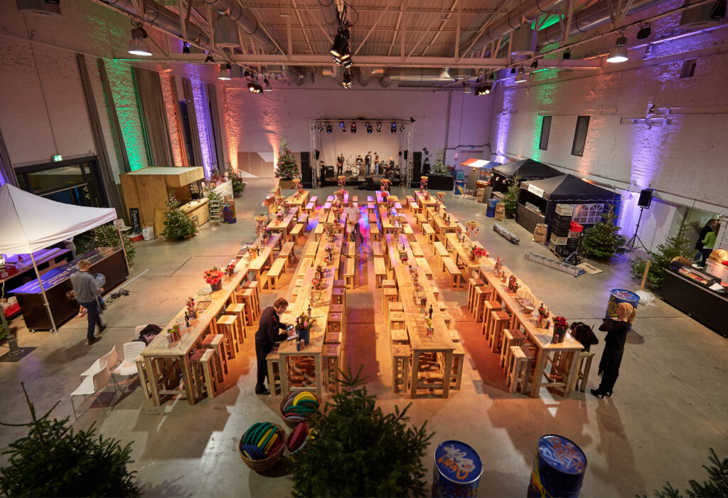 Großer Indoor-Veranstaltungsraum im Dock 2 in Köln für Events mit langen Holztischen, festlicher Dekoration und farbenfroher Beleuchtung.