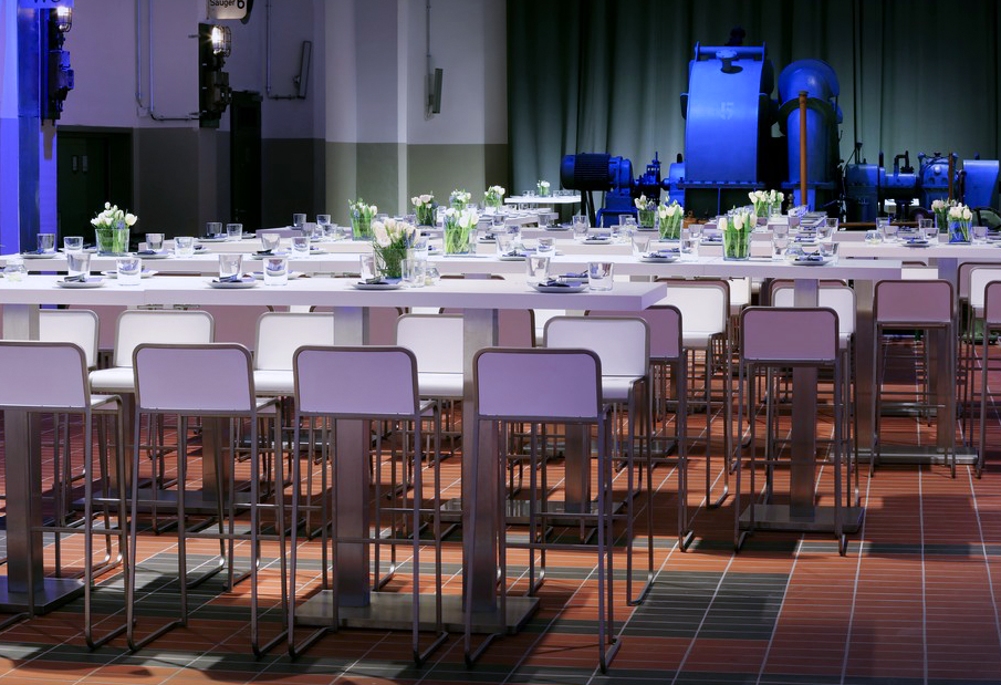 Moderne Esstische mit weißen Stühlen, Glaswaren und Tulpen-Tischdekorationen schaffen eine elegante Atmosphäre für das Catering im einzigartigen Industrieambiente der Grand Hall Zollverein.