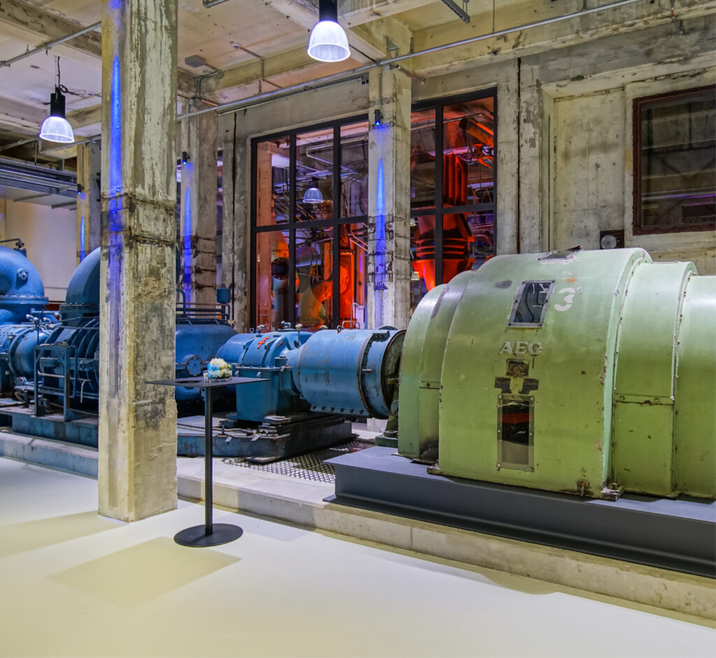 Große historische Industriemaschinen mit Rohren und Generatoren in einer Fabrikhalle aus Beton erinnern an die beeindruckende Atmosphäre des Caterings in der Grand Hall Zollverein.