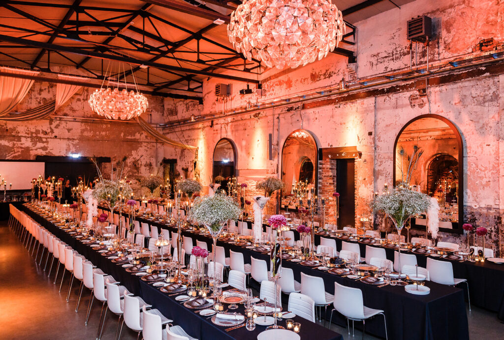 Eleganter Bankettsaal mit langen Tischen, die für das Abendessen gedeckt sind, floralen Tafelaufsätzen und warmer, dramatischer Beleuchtung - ideal für diejenigen, die Eventlocations Köln für einen besonderen Anlass mieten möchten.