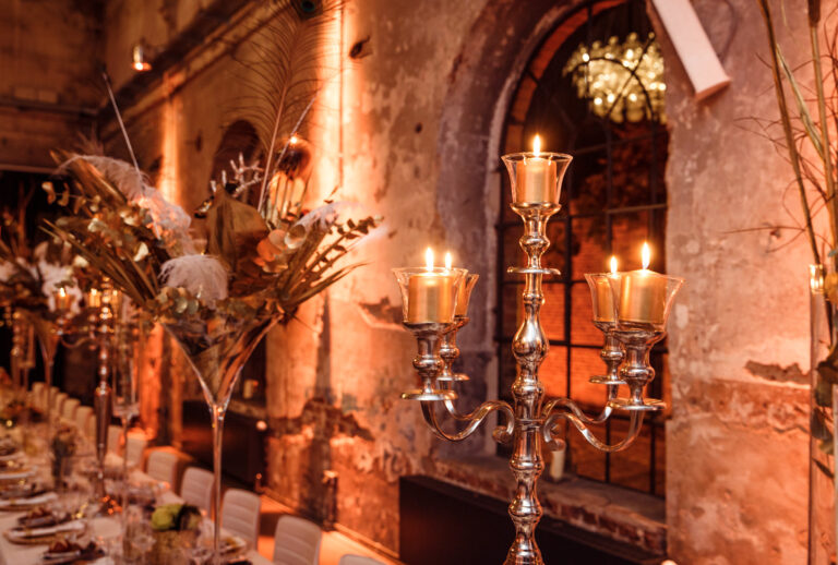 Elegante Tischdekoration mit einem silbernen Kandelaber und Blumenarrangements in einem warm beleuchteten, rustikalen Veranstaltungsort – perfekt kuratiert von Harbour Club Events und Catering.