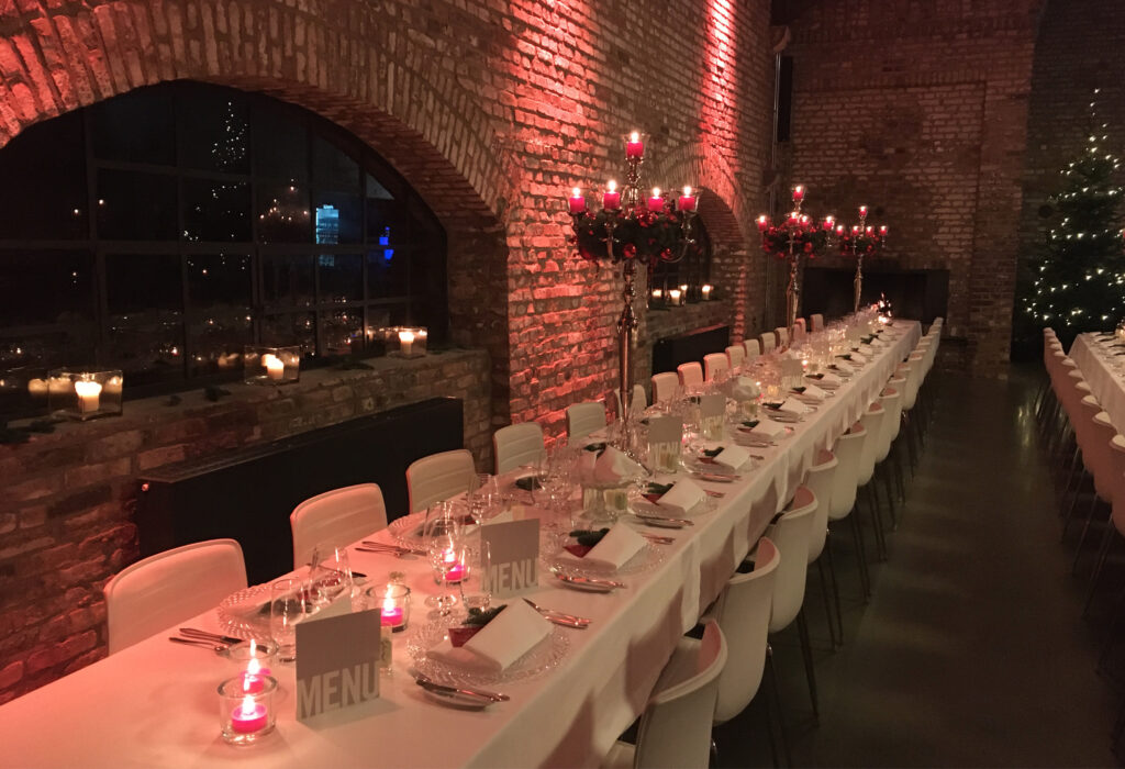 Ein langer, eleganter Esstisch, gedeckt für ein formelles Abendessen in einem Lokal mit Backsteinwänden und Kerzenlicht von Harbour Club Events und Catering.