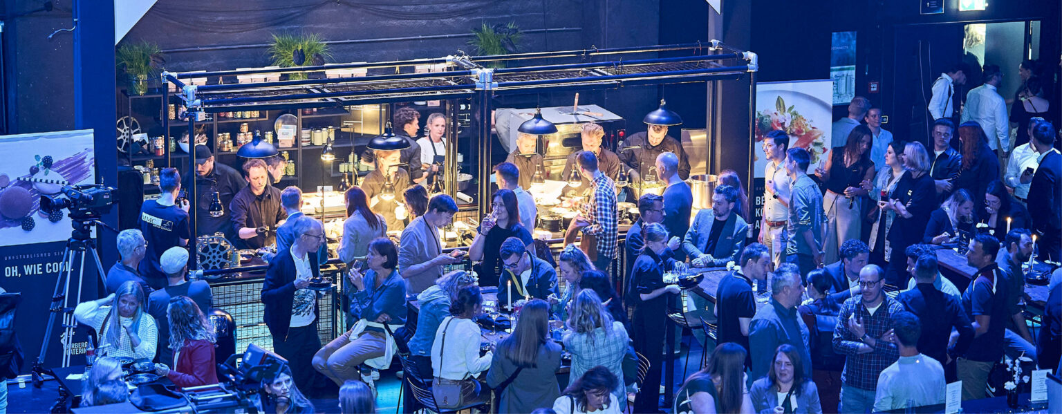 Viele Menschen speisen und unterhalten sich in einem geschäftigen, modernen Indoor-Food-Markt, in dem Köche Gerichte zubereiten – ideal für Zusammenkünfte im Studio 50 als Eventlocation.