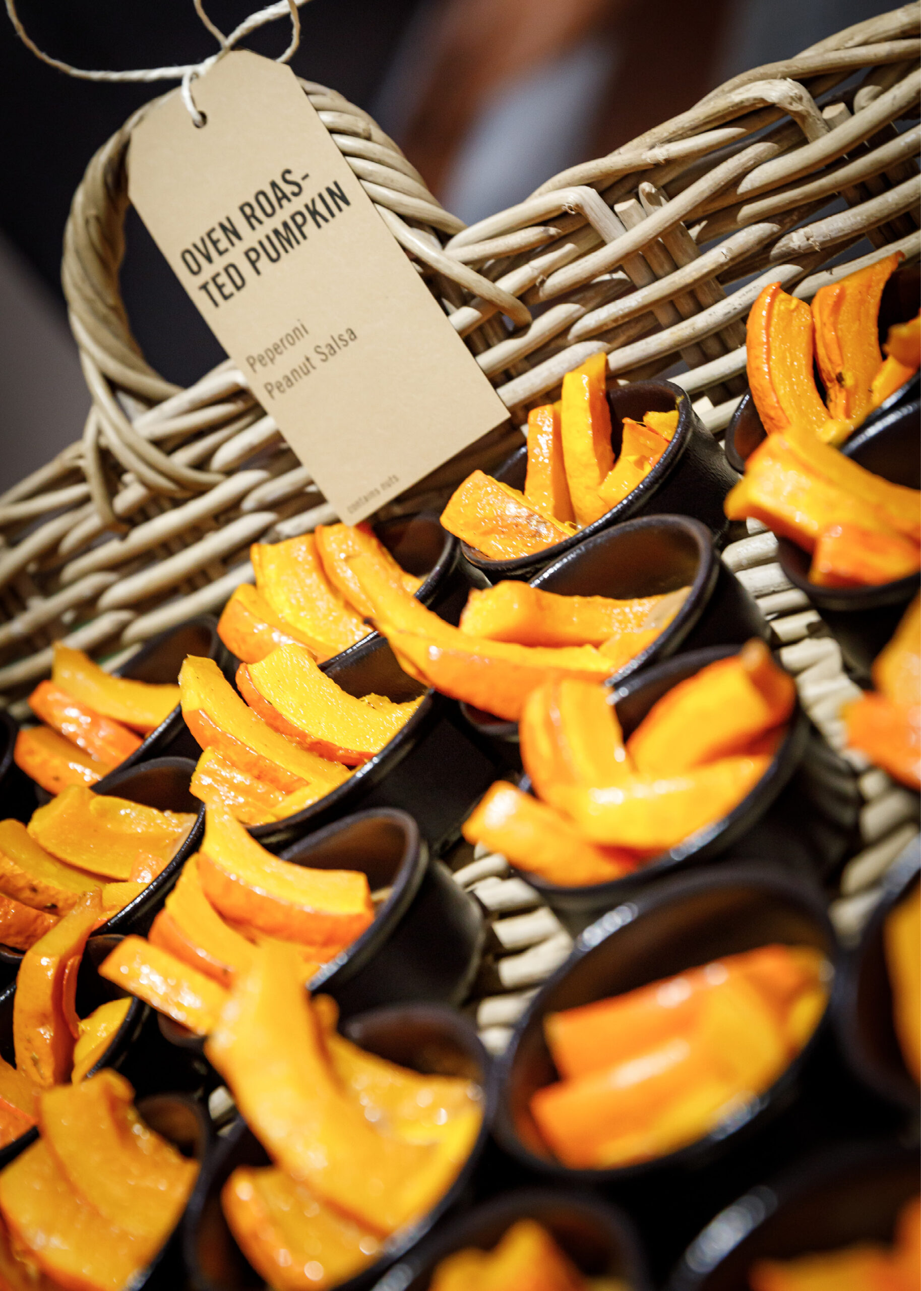 Kleine Becher gefüllt mit im Ofen gerösteten Kürbisscheiben werden in einem Weidenkorb mit Etikett arrangiert.
