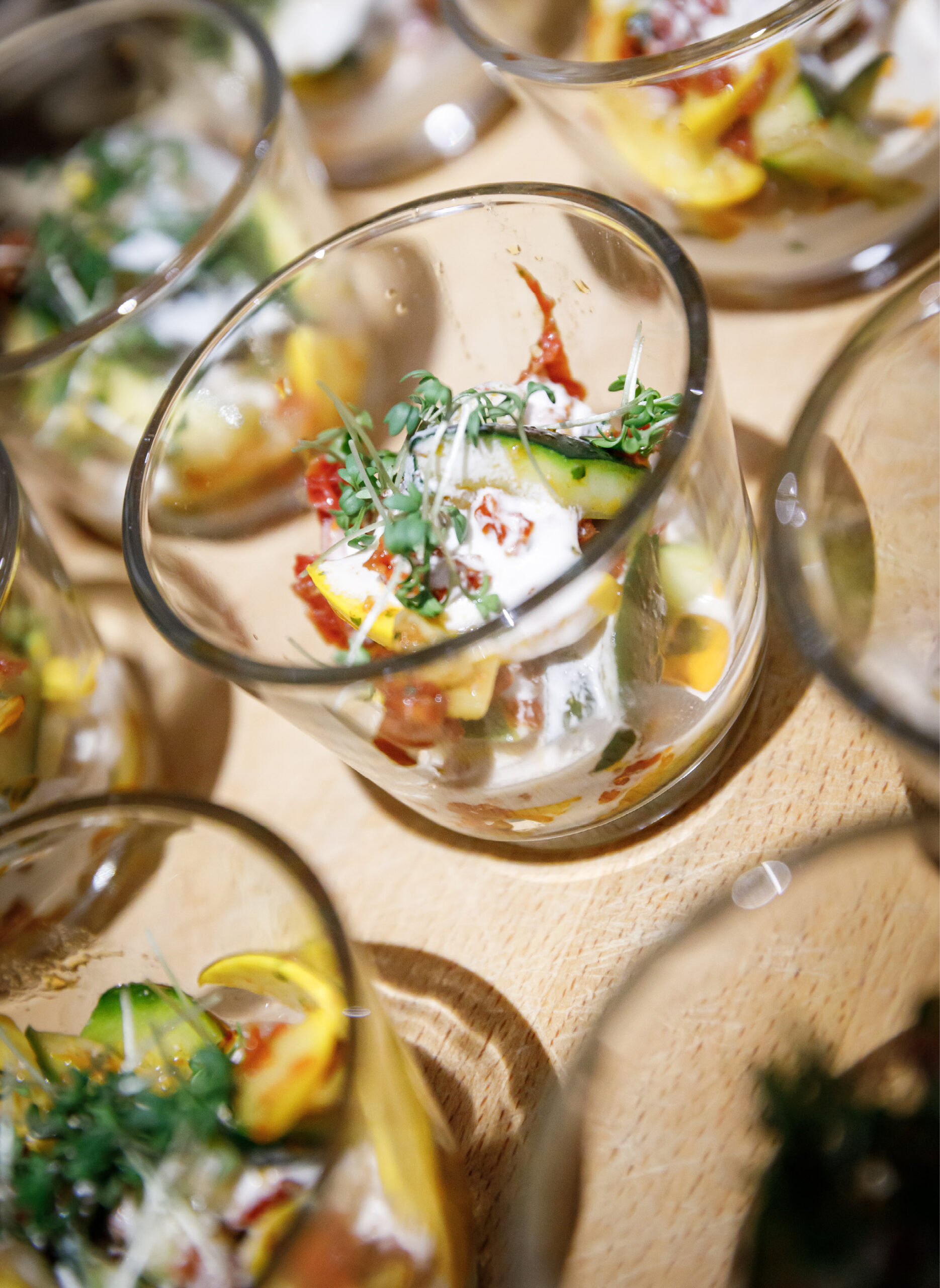 Kleine Glasbecher gefüllt mit buntem Gemüsesalat und garniert mit frischen Kräutern auf einer Holzunterlage.