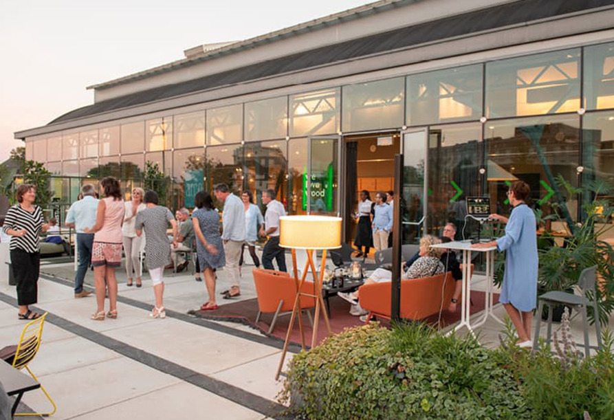 Menschen treffen sich bei Sonnenuntergang auf einer modernen Außenterrasse mit Glaswänden und Terrassenmöbeln und genießen die einzigartige Atmosphäre der Design Post als Eventlocation.