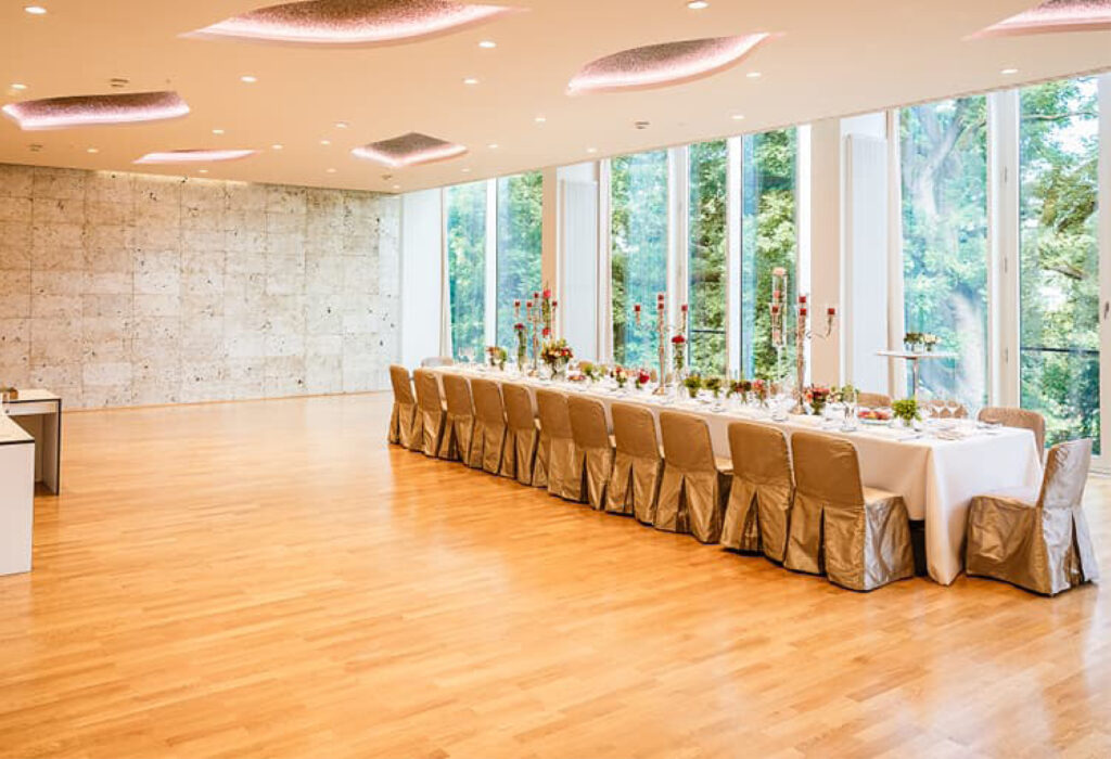 Ein langer, elegant gedeckter Esstisch für eine Veranstaltung in einem hellen Raum mit großen Fenstern und Holzboden – perfekt für das Catering in der Flora Köln.