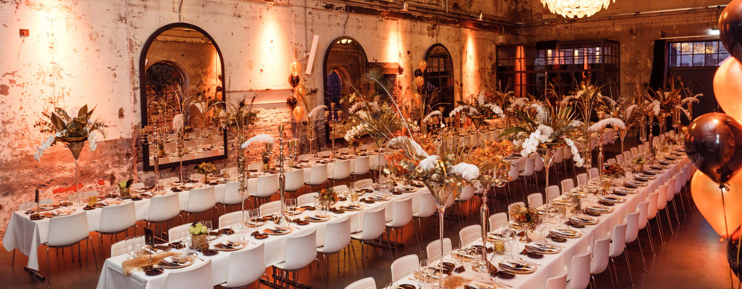 Lange Banketttische für eine Veranstaltung in einem rustikalen, warm beleuchteten Veranstaltungsort mit eleganten Blumengestecken von Harbour Club Events und Catering.
