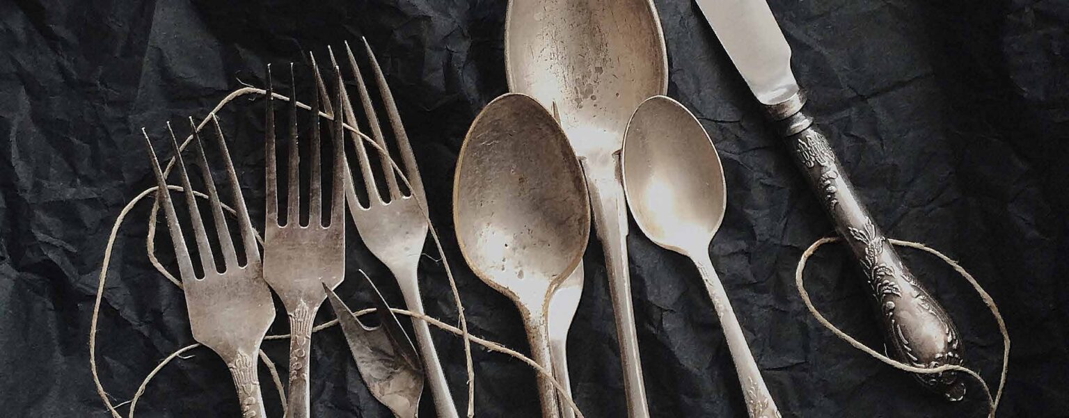 Verschiedene Vintage-Silberbestecke, darunter Gabeln, Löffel und ein Messer, auf einem dunklen strukturierten Hintergrund.