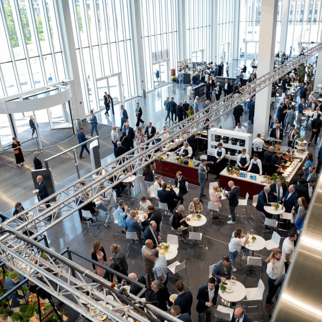 Ein geschäftiges, modernes Atrium, in dem Menschen während einer professionellen Veranstaltung Kontakte knüpfen und an Tischen speisen können.
