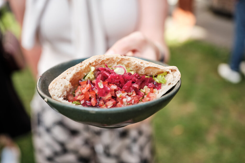 Person hält ein mit frischem Gemüse und Salat gefülltes Pita-Brot, präsentiert auf einem dunkelgrünen Teller.