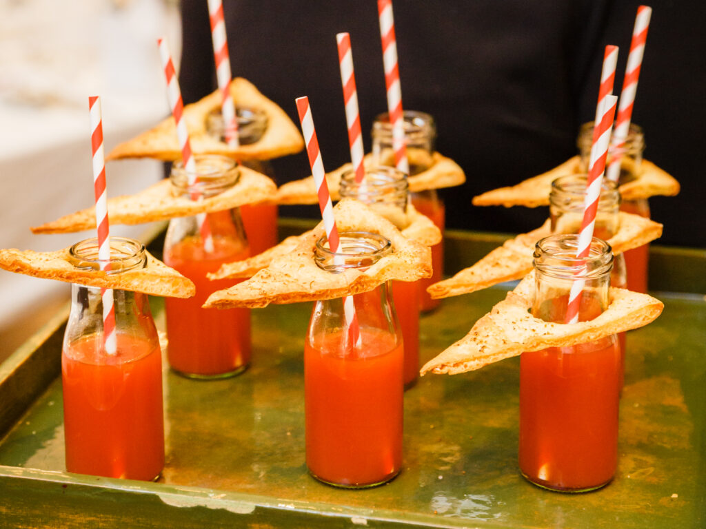 Miniflaschen Tomatensuppe mit rot gestreiften Strohhalmen und Toastdreiecken obendrauf, serviert auf einem Tablett.