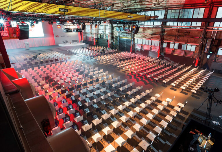 Geräumiger, moderner Konferenzsaal im Fredenhagen als Veranstaltungsort mit Reihen leerer weißer Stühle vor einer Bühne mit großer Leinwand.