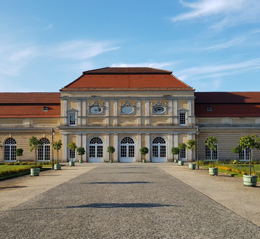 Elegantes historisches Gebäude mit Bogenfenstern, rotem Dach und Topfbäumen entlang eines Steinwegs – perfekt für alle, die Eventlocations in Köln mieten möchten.