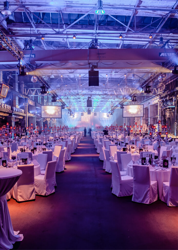 Eleganter Bankettsaal im Fredenhagen als Veranstaltungsort mit runden Tischen, weißen Stühlen und violetter Beleuchtung für eine formelle Veranstaltung.