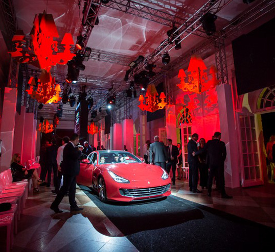 Bei einer Indoor-Veranstaltung in der Orangerie Charlottenburg für Hochzeiten wird ein roter Sportwagen ausgestellt, mit geselligem Beisammensein und dramatischer roter Beleuchtung.