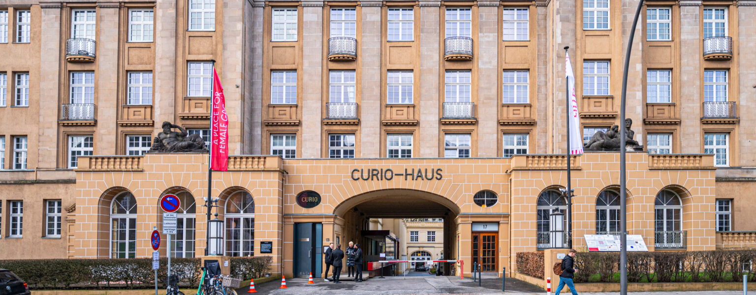 Fassade des Curio-Hauses mit gewölbtem Eingang, Statuen und draußen stehenden Menschen.