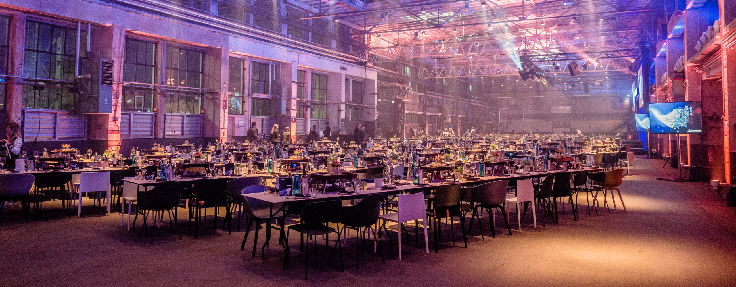 Großer, dekorierter Bankettsaal im Fredenhagen als Veranstaltungsort mit Reihen von Tischen und Stühlen, die für eine Veranstaltung gedeckt sind und wunderschön mit farbenfroher Beleuchtung von unten beleuchtet werden.