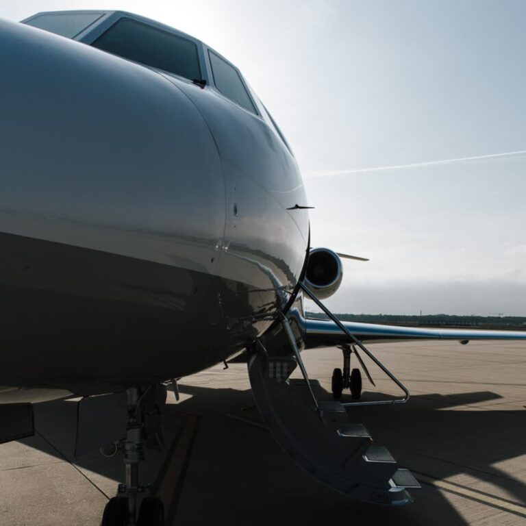 Nahaufnahme eines Privatjets mit offener Treppe auf dem Rollfeld eines Flughafens bei klarem Himmel.