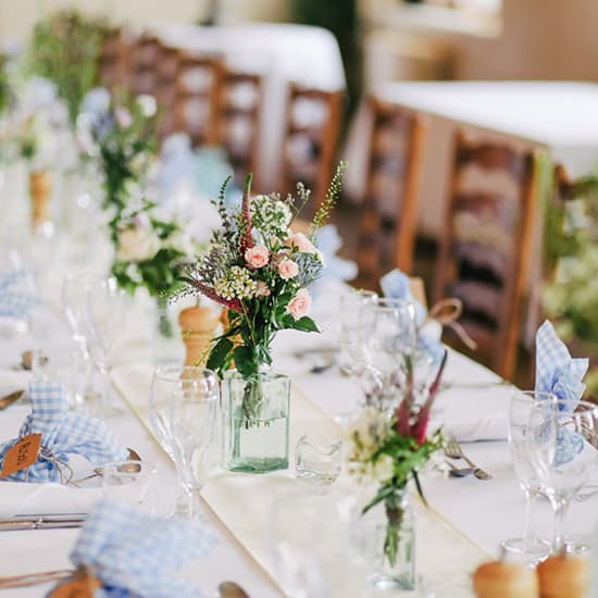 Elegante Tischdekoration mit Wildblumen-Tischdekorationen, Glaswaren und karierten Servietten bei einer Veranstaltung oder Hochzeit.