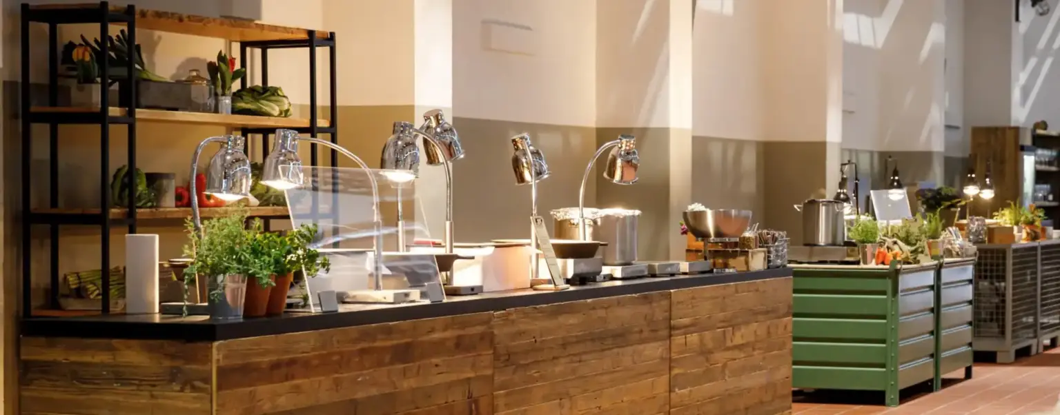 Buffettheke mit Speisenwärmern, Geschirr und Topfpflanzen in einem gut beleuchteten, modernen Essbereich.