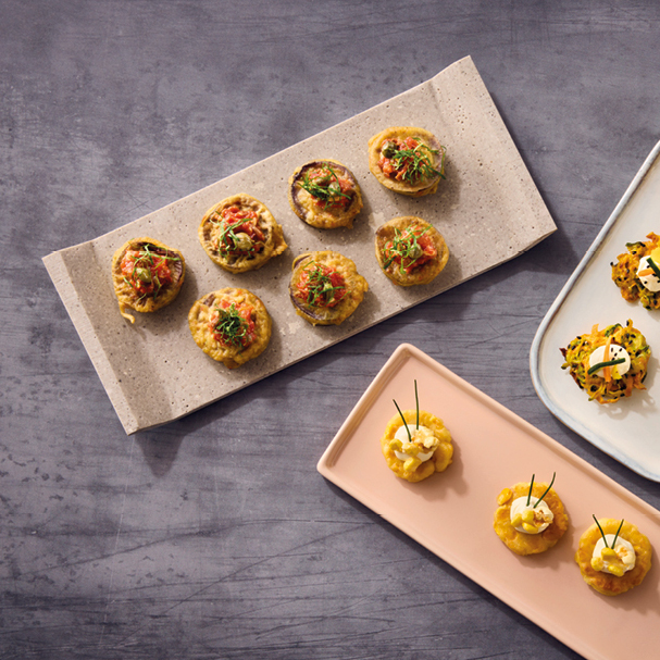 Drei Teller mit verschiedenen mundgerechten Vorspeisen, ordentlich auf einer grauen Oberfläche angeordnet.