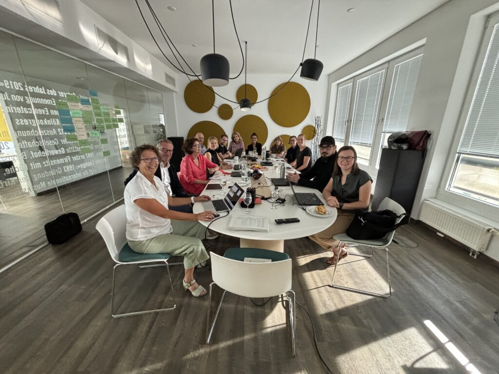 Bild von 11 Kirberg Catering Mitarbeitern, die bei einem Gemeinwohl-Ökonomie-Workshop um einen Konferenztisch herum sitzen.