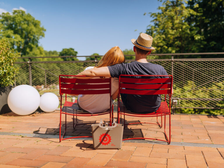 Ein Paar sitzt auf roten Stühlen im Freien und genießt die Sonne mit dem Grün im Hintergrund.