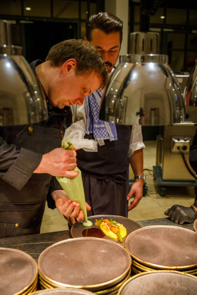 Zwei Köche, die Gourmetgerichte anrichten, ein Koch, der eine Soße auf ein Gericht in einer professionellen Küche aufträgt.