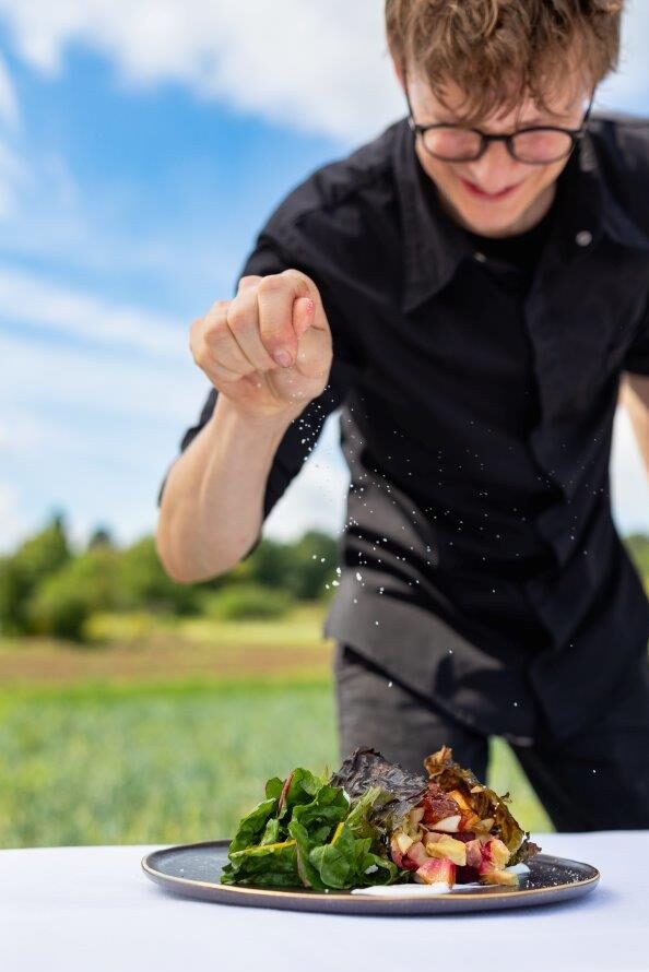 Person, die einen Salat im Freien mit Gewürzen bestreut, mit Grünzeug und blauem Himmel im Hintergrund.