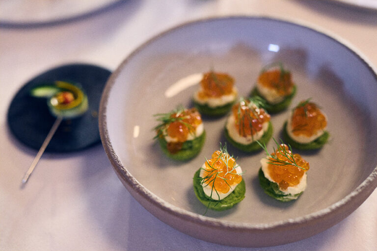 Eine Schale mundgerechter Canapés mit Orangenkaviar und Dill, serviert neben einem kleinen Teller mit einer Garnitur - ein eleganter Genuss, der an die Kunstfertigkeit von Philara 14 Places erinnert.